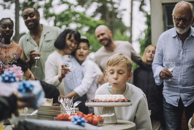 Boy blowing candle on cake during birthday celebration with family