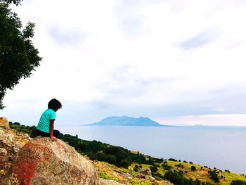 Man standing on rock looking at mountain against sky