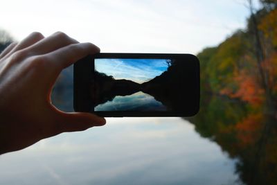 Close-up of hand holding mobile phone against sky