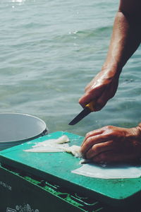 Fisherman cutting fish against sea