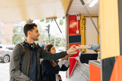 Young man standing with female friend receiving meal from food truck in city