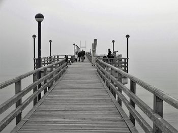 People on pier over sea against sky during foggy weather