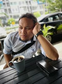 Thoughtful mid adult man with coffee sitting at sidewalk cafe