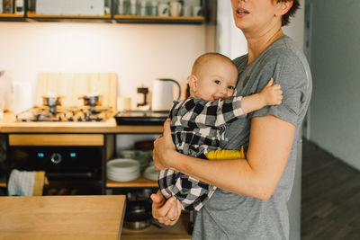A mother holds her daughter in her arms in the kitchen.