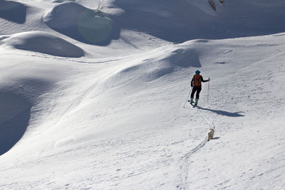 Full length of woman skiing with mammal walking on snow covered mountain