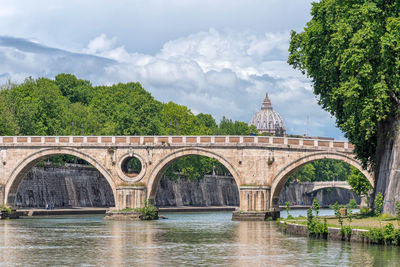 Arch bridge over river against cloudy sky