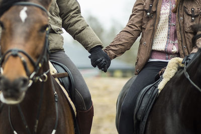 Low section of couple holding hands while riding horses