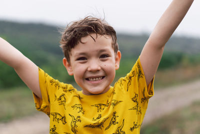 A six year old boy smiles at the camera in the park