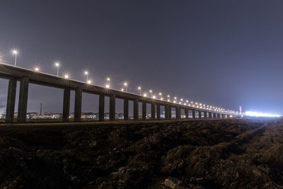 Illuminated bridge over street against sky at night