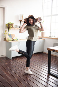 Portrait of smiling young woman standing on one leg on floor at home