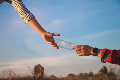 Low angle view of hand holding hands against sky