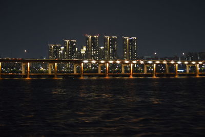 Illuminated buildings by river against clear sky at night