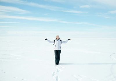 Woman with arms outstretched standing on snowy field against sky