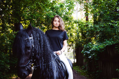 Portrait of young woman riding with horse amidst trees