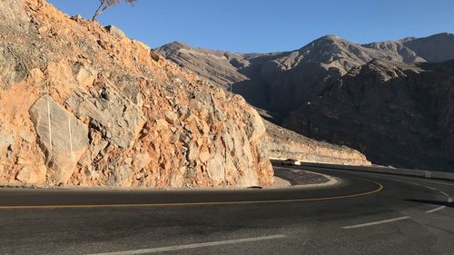 Road leading towards mountains against clear sky