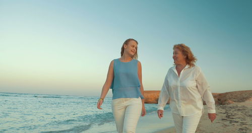 Women standing on beach against clear sky