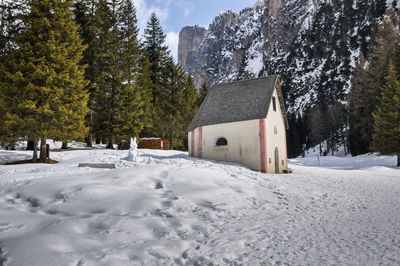 House on snow covered field by trees and buildings