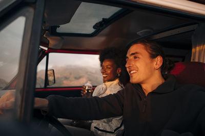 Smiling young man driving van with female friend on vacation