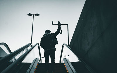 Low angle view of silhouette man standing by railing against sky