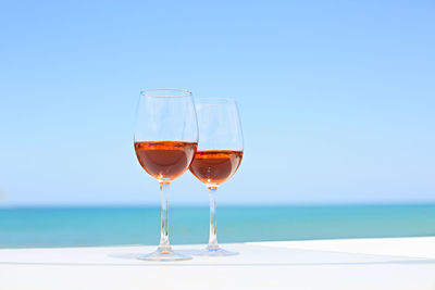 Wineglass on table by sea against clear blue sky