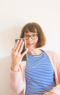 Smiling woman using smart phone against wall