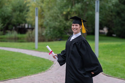 Portrait of woman wearing graduation gown standing on field