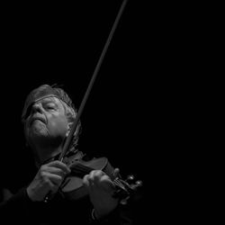 Senior man playing violin against black background