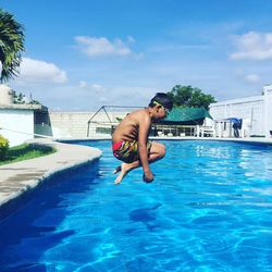 Side view of shirtless boy jumping in swimming pool against sky