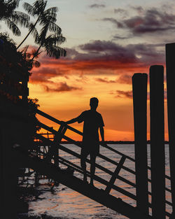 Low angle view of silhouette man standing by railing against sky during sunset
