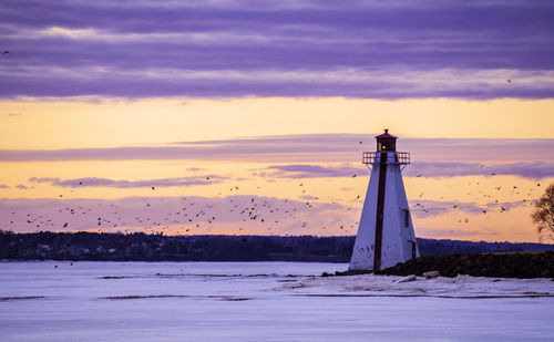 Lighthouse by sea against sky during sunset