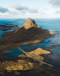 High angle view of rock mountain by sea against cloudy sky