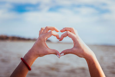 Cropped hands of woman making heart shape at beach