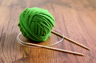 Knitting needles with ball of green wool on table