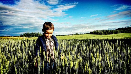 Boy walking in wheat field against sky