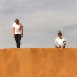 Friends on sand against sky during sunny day