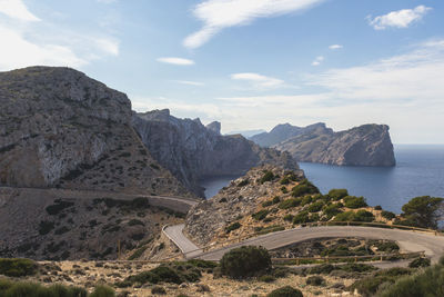 Mountain roads by sea against cloudy sky on sunny day