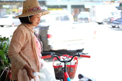 Close-up of mature woman wearing hat standing with bicycle