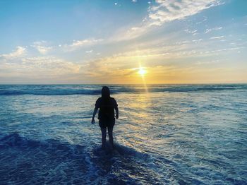 Rear view of silhouette man standing at beach during sunset