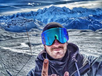 Portrait of man in ski goggles gesturing against snow covered mountains