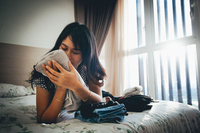 Young woman holding textile while lying on bed at home