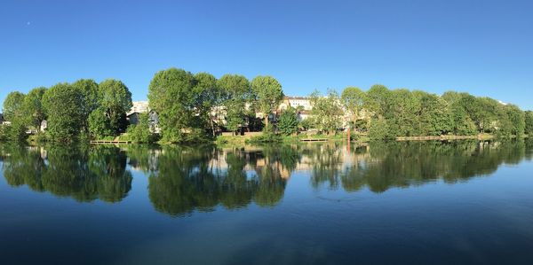 Scenic view of lake by trees against clear blue sky