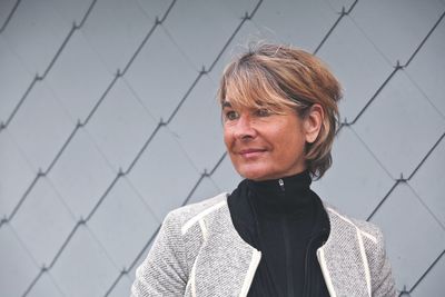 Close-up of smiling thoughtful woman standing by patterned wall