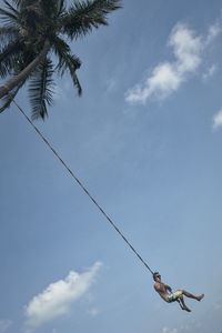 Low angle view of man swinging against sky