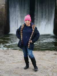 Full length portrait of smiling woman standing against waterfall