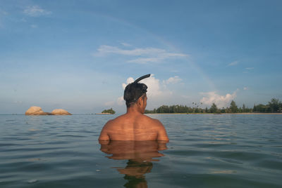 Rear view of shirtless man in sea against sky on sunny day