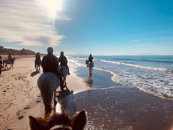 People riding on beach against sky