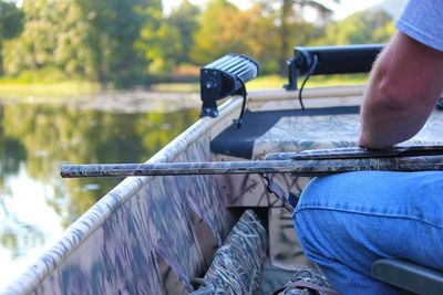 Midsection of man with rifle sitting in boat on lake