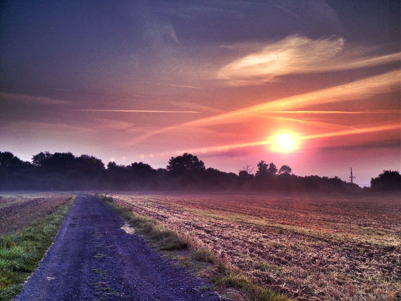 sunset, the way forward, tranquil scene, tranquility, sun, sky, scenics, beauty in nature, landscape, nature, road, diminishing perspective, tree, dirt road, sunlight, field, sunbeam, vanishing point, water, idyllic