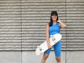 Portrait of young woman amused by the wall with a skateboard