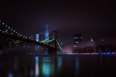 Illuminated bridge over river in city at night